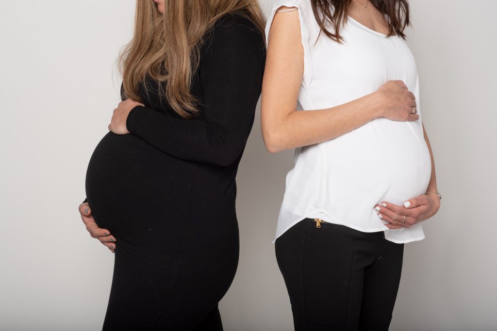 Two pregnant women standing back-to-back cradling their bumps