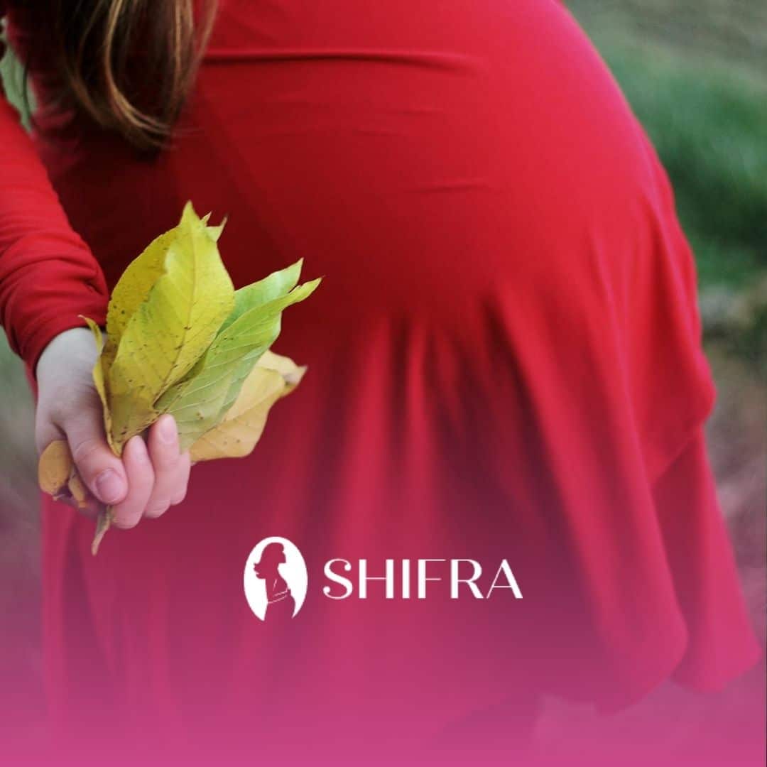 Pregnant woman considering to get an abortion wearing a in red dress holding green leaves outdoors.