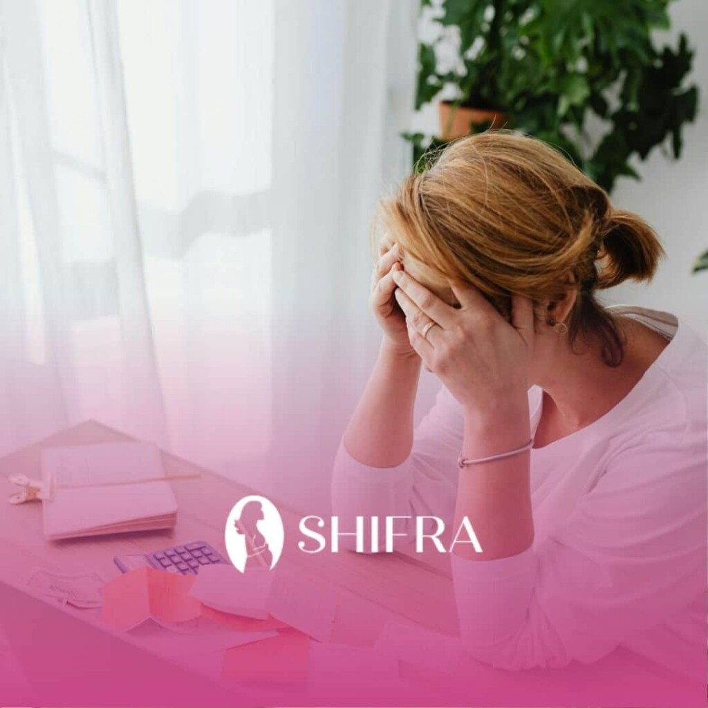 A pregnant woman in white stressed at desk with bills and receipts, experiencing financial strain.