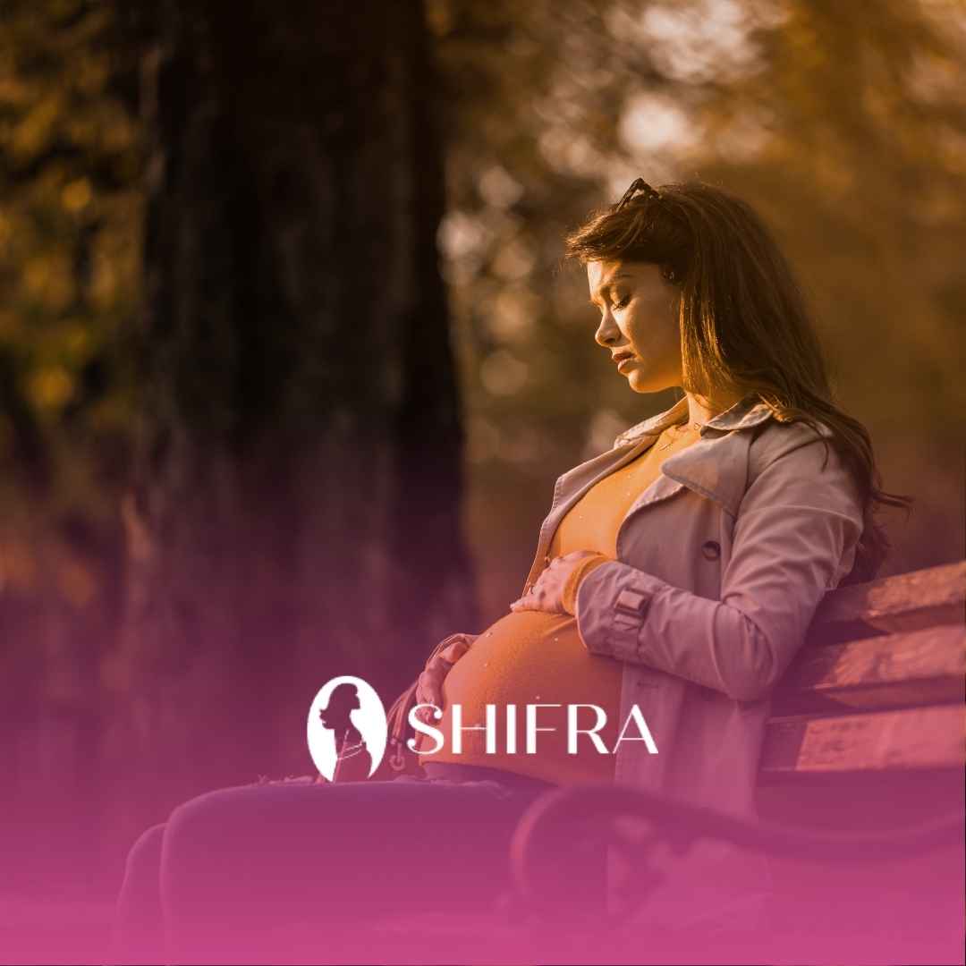 Pregnant woman sitting on a park bench, cradling her belly, with a serene expression. Sunlight filters through trees, creating a warm, peaceful scene.