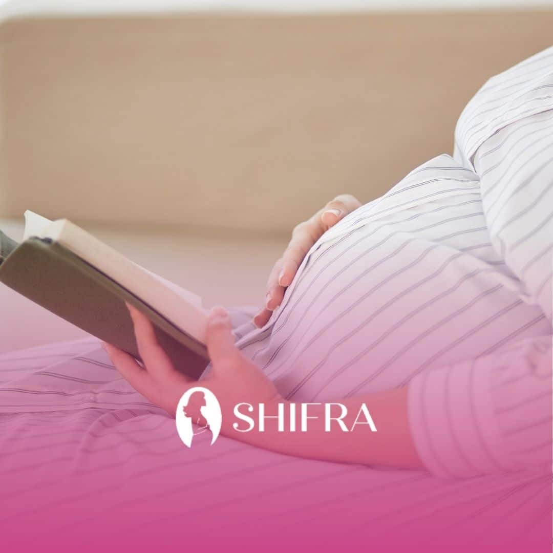 Pregnant person in a striped dress, sitting and holding a book. The setting is calm and relaxed.