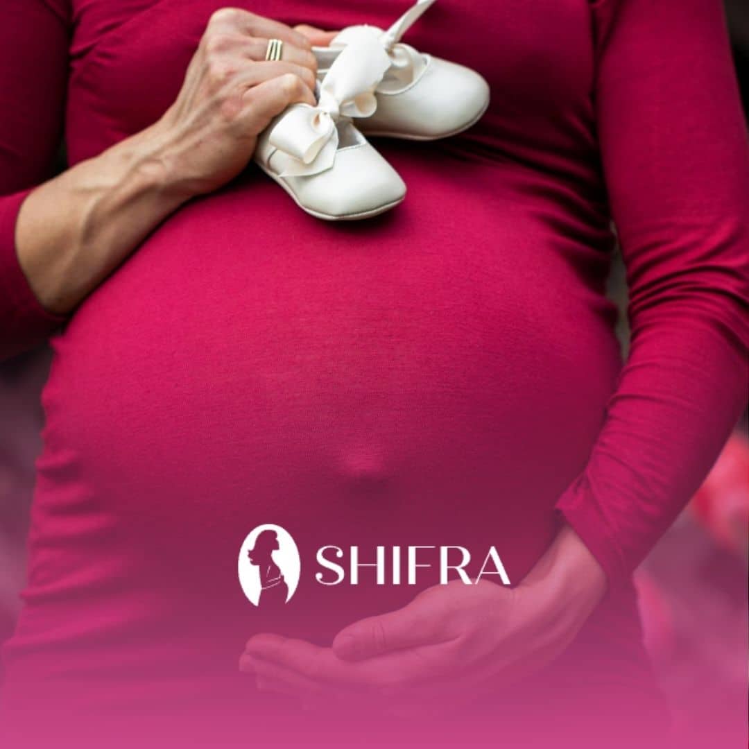 Pregnant woman having unplanned pregnancy wearing a red dress while holding baby shoes on her belly.