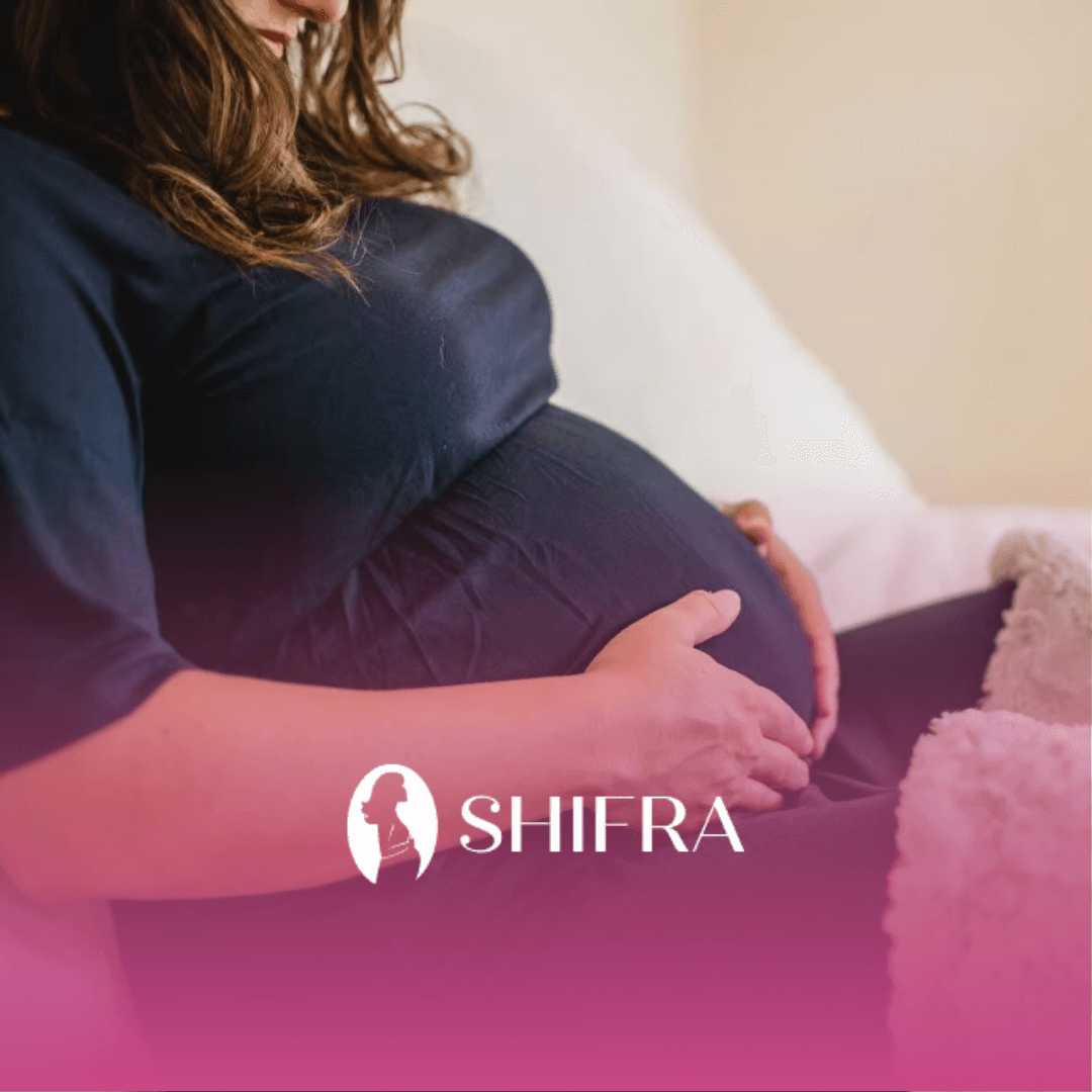 A jewish pregnant woman gently holding her belly while sitting on a bed at home, worrying about parenthood.